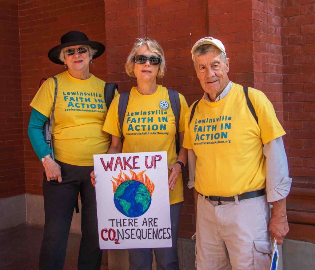 Three adults from Lewinsville Presbyterian church wearing matching t-shirts and holding a sign